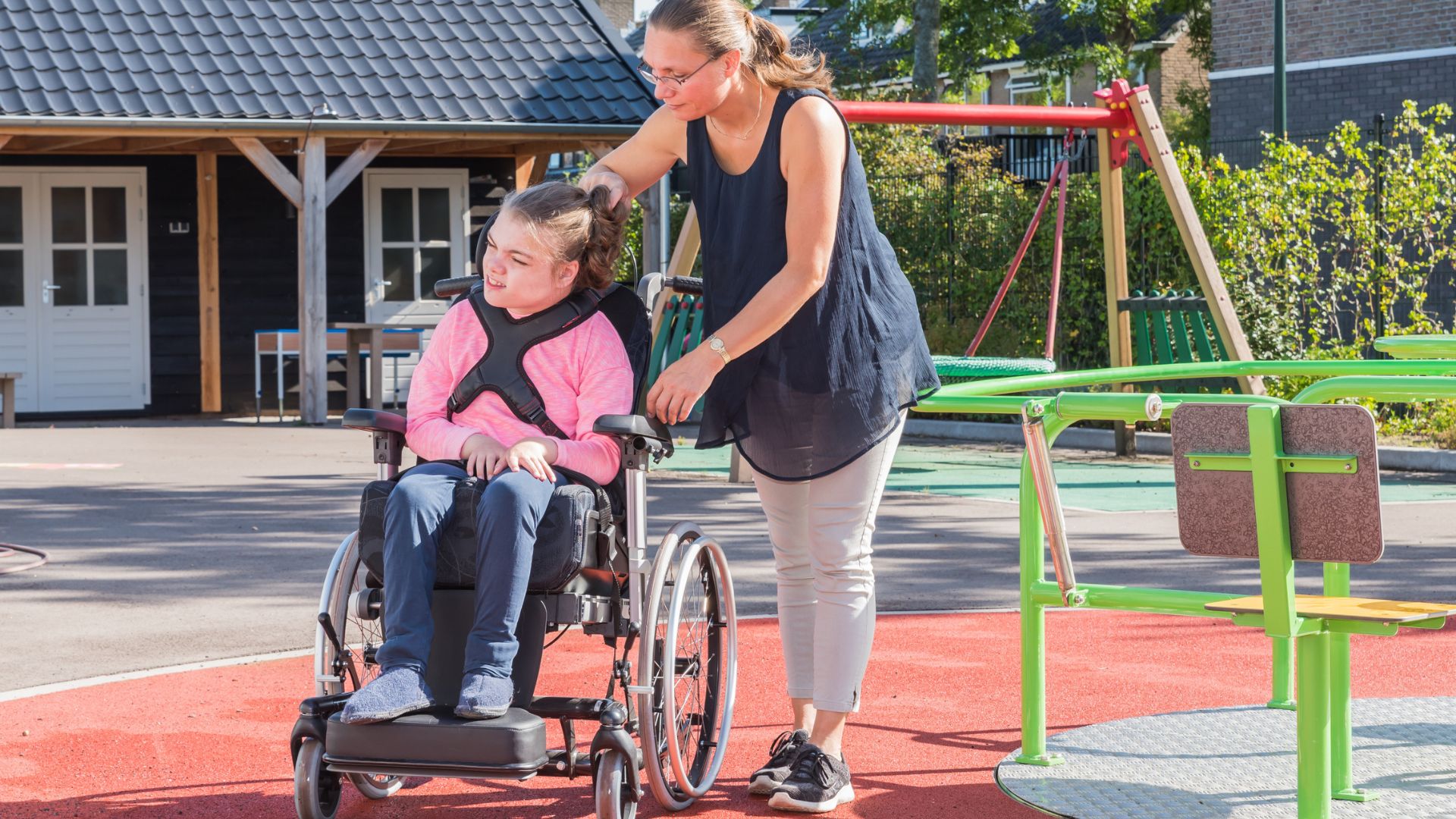 Caregiver pushing child in wheelchair at park.
